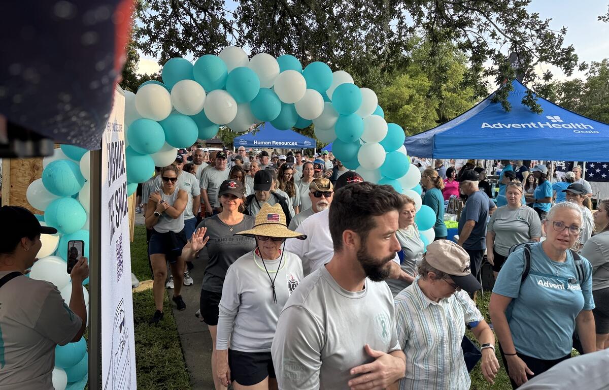 Crowd of participants walking through teal and white balloon arch at PTSD Awareness Walk in Ocala.