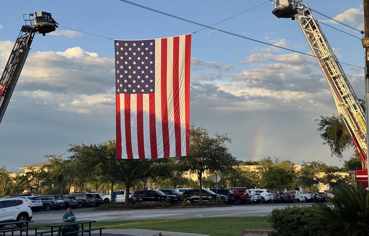 American flag suspended between two fire trucks with a faint rainbow in the background in Ocala, Florida.