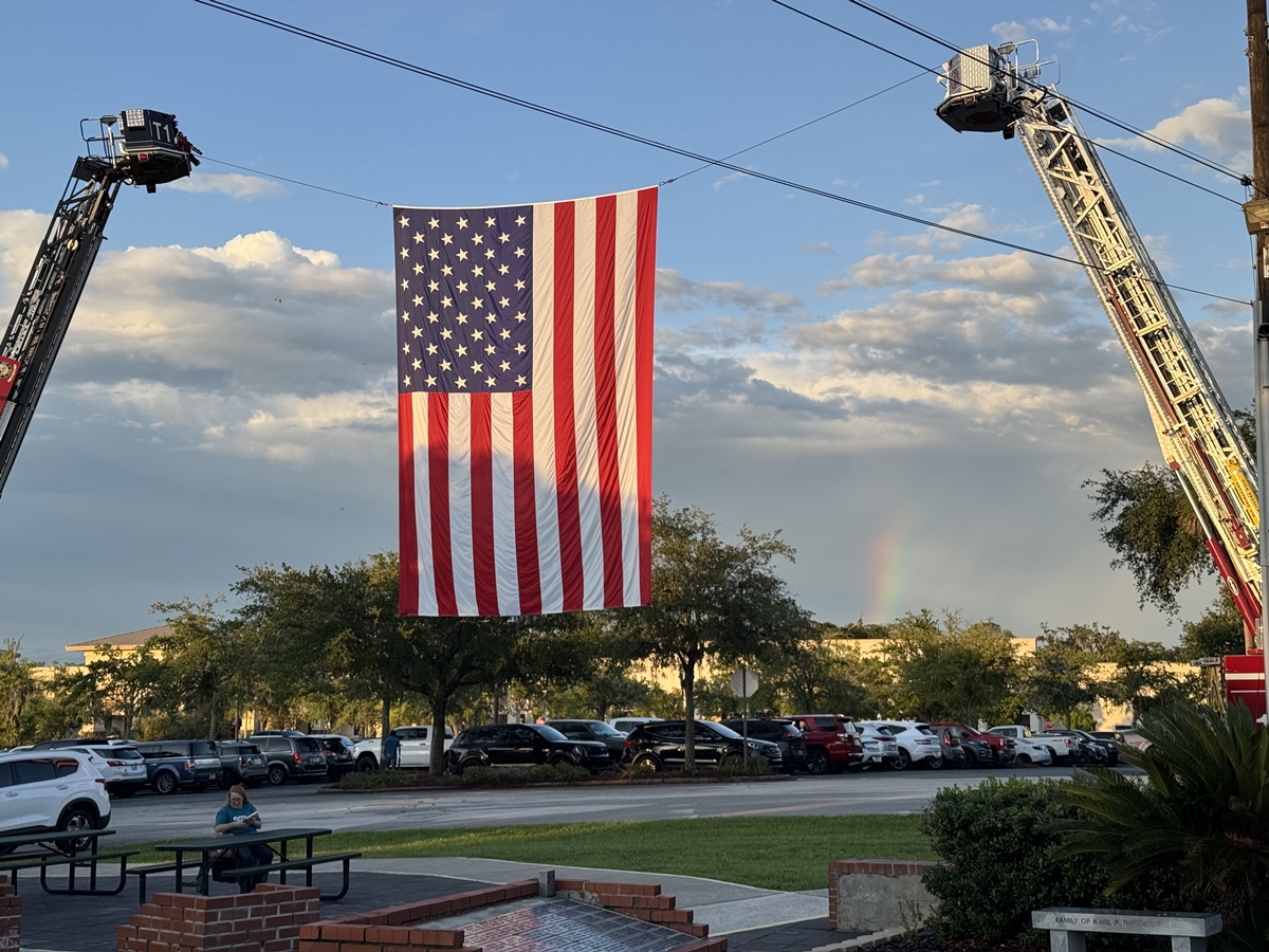 American flag suspended between two fire trucks with a faint rainbow in the background in Ocala, Florida.