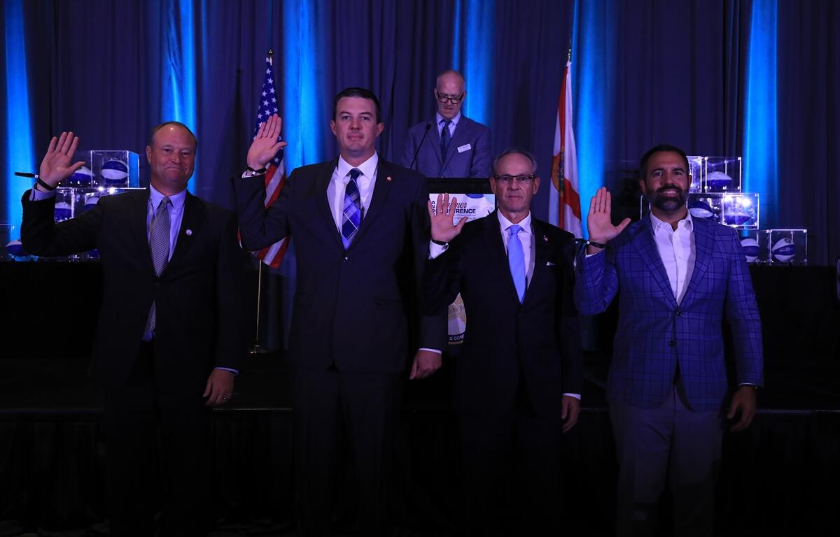 Four Florida clerks of court raise their right hands as they are sworn in on stage with blue lighting and American and Florida flags in the background.