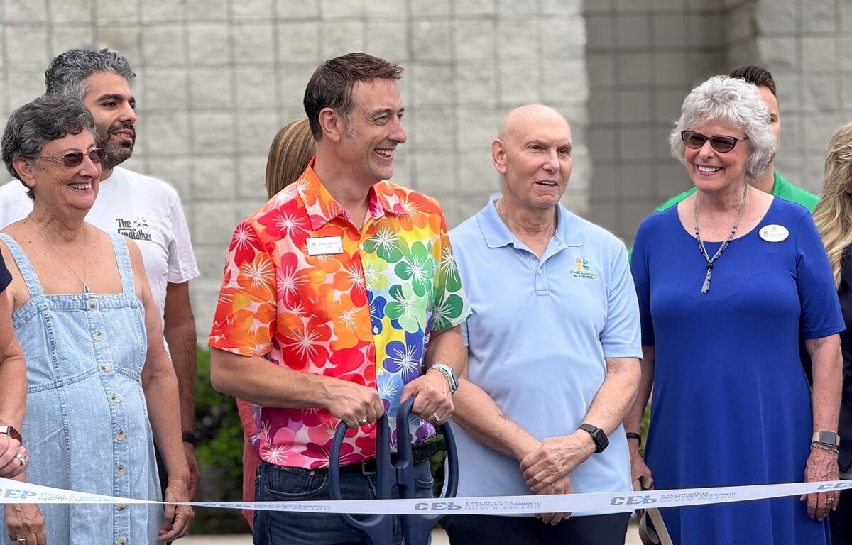 Robb Harrison stands with a group of supporters, including family, team members, and a dog, in front of his realty office during the ribbon-cutting event in Ocala.