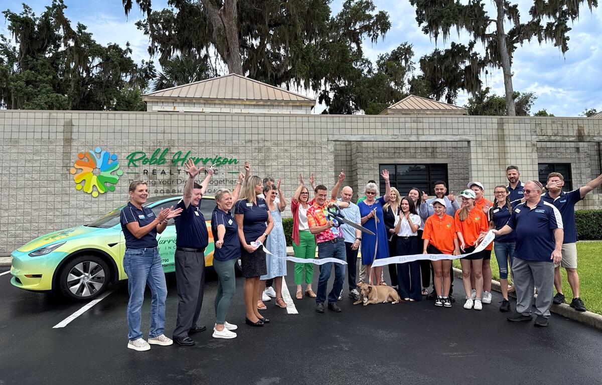 Robb Harrison cuts a ceremonial ribbon with oversized scissors while surrounded by supporters and CEP members outside the new Robb Harrison Realty office in Ocala.