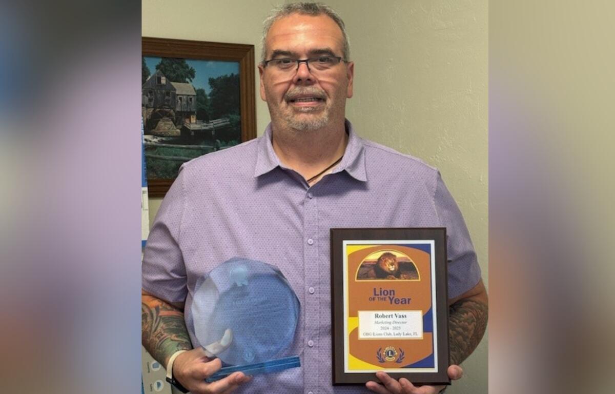Robert Vass smiling while holding his Lion of the Year plaque and Helen Keller Award in an indoor setting.