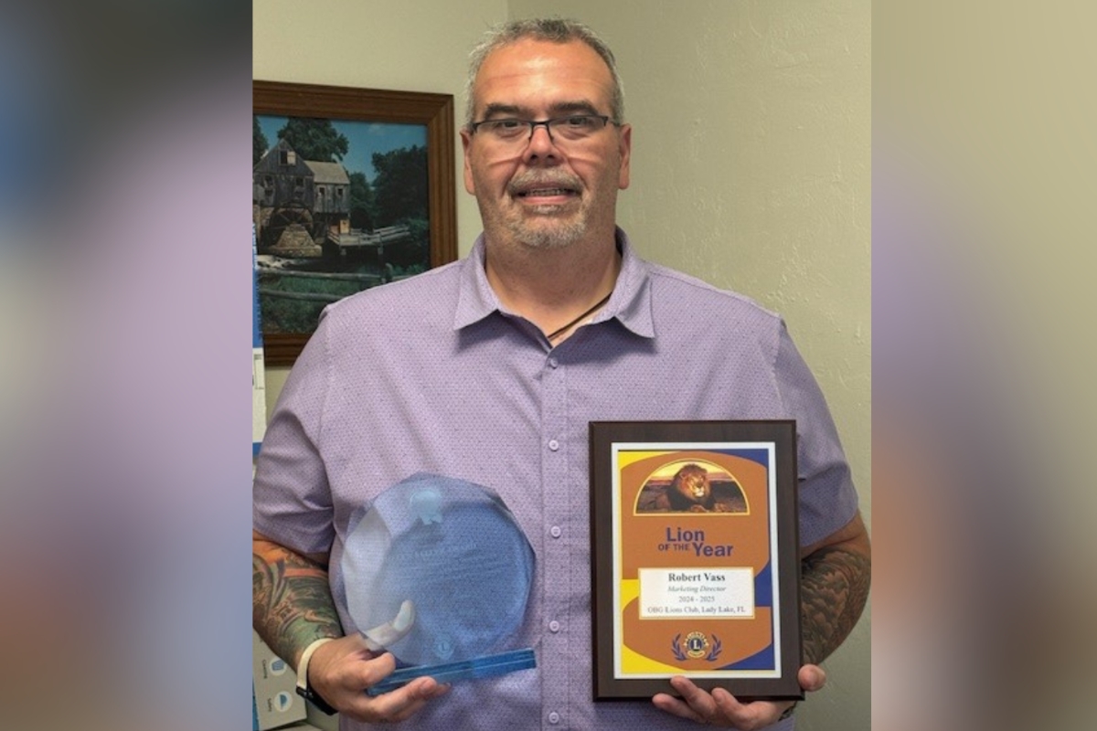 Robert Vass smiling while holding his Lion of the Year plaque and Helen Keller Award in an indoor setting.