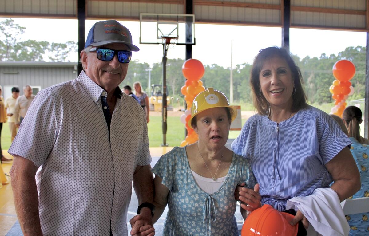 A TLC member stands between two adults, holding hands and smiling inside the pavilion decorated for the ceremony.