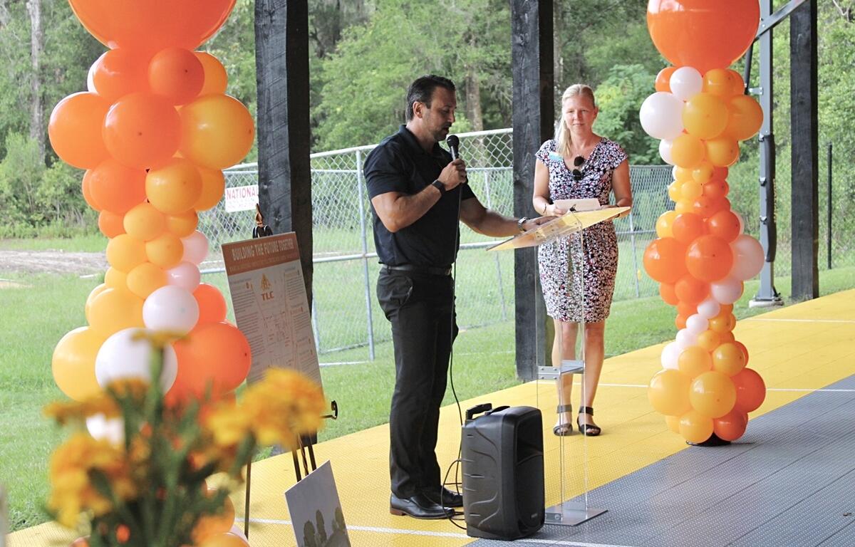 Ocala Mayor Ben Marciano speaks at a podium decorated with balloons during the TLC expansion ceremony, with a woman standing beside him.
