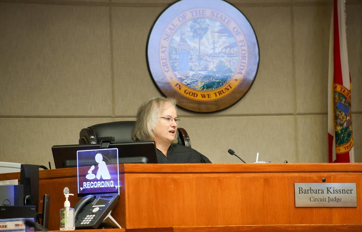 Judge Barbara Kissner speaks from the bench in a Florida courtroom with the state seal and flag visible behind her.