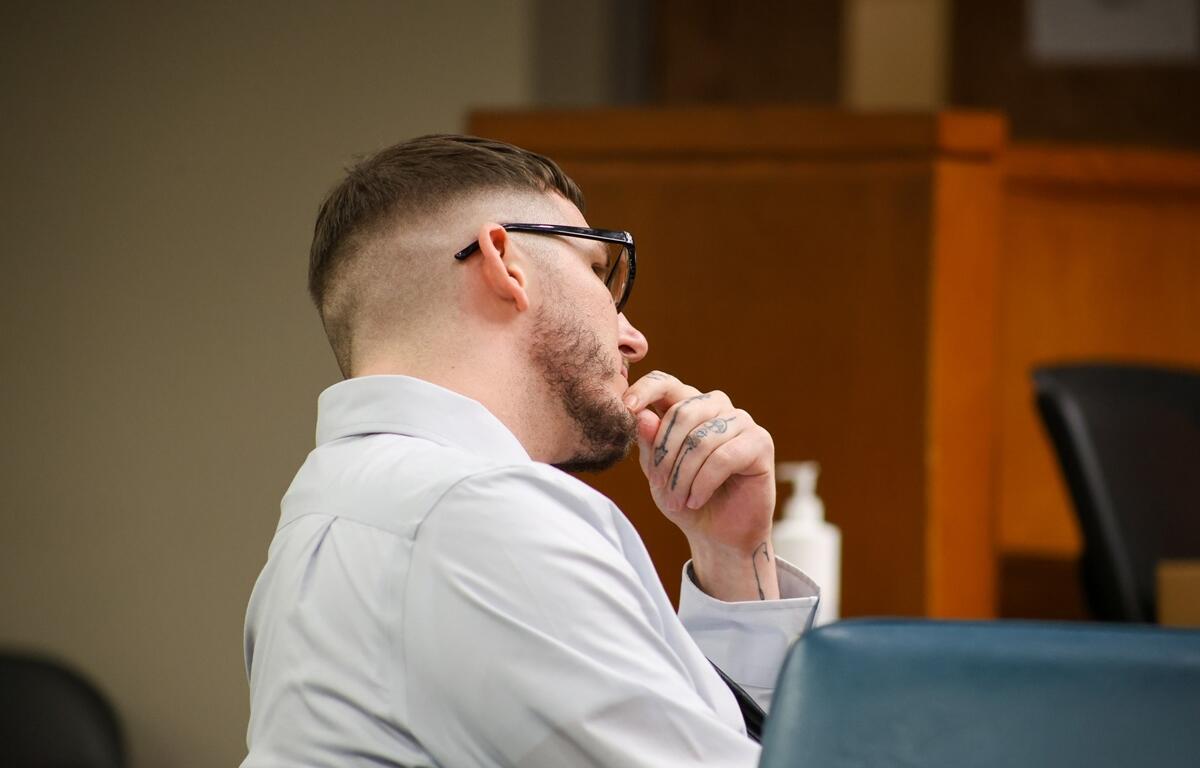 Travis Ray Thompson seated in a courtroom, resting his hand on his chin during his murder trial.