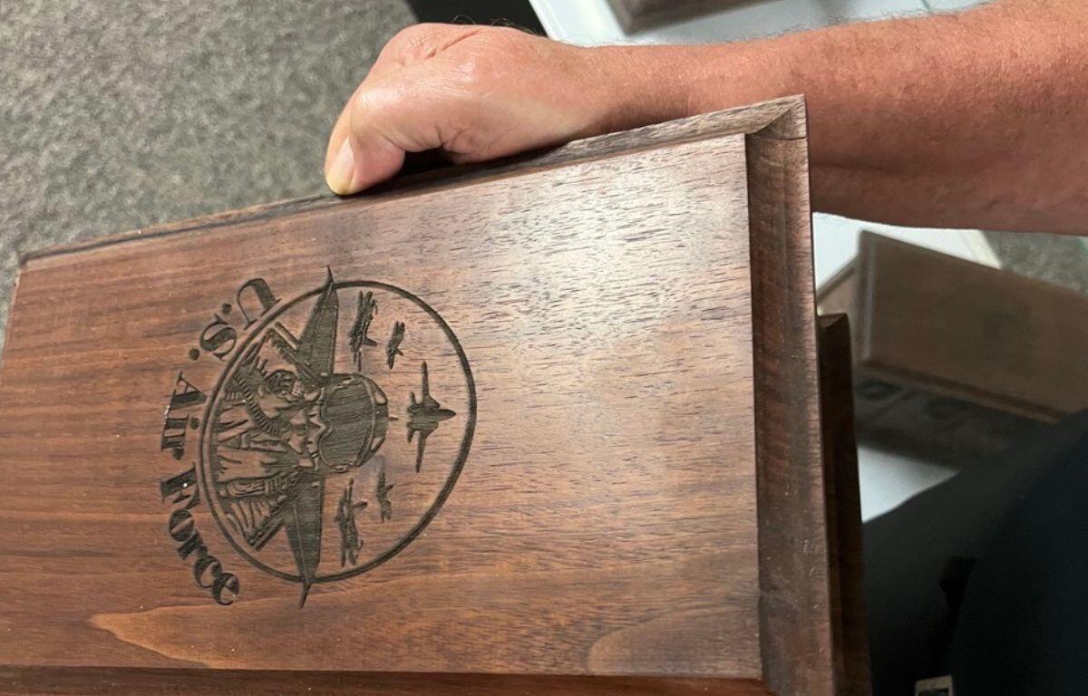 A man hand on the top of a wooden box, with an etching in the center of the top of the box.