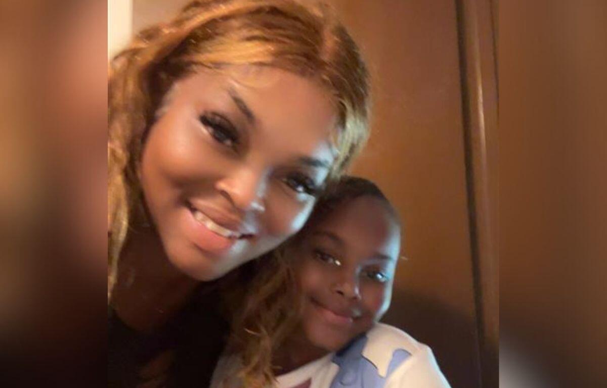 A woman and a young girl are smiling warmly together in a close-up selfie taken indoors.