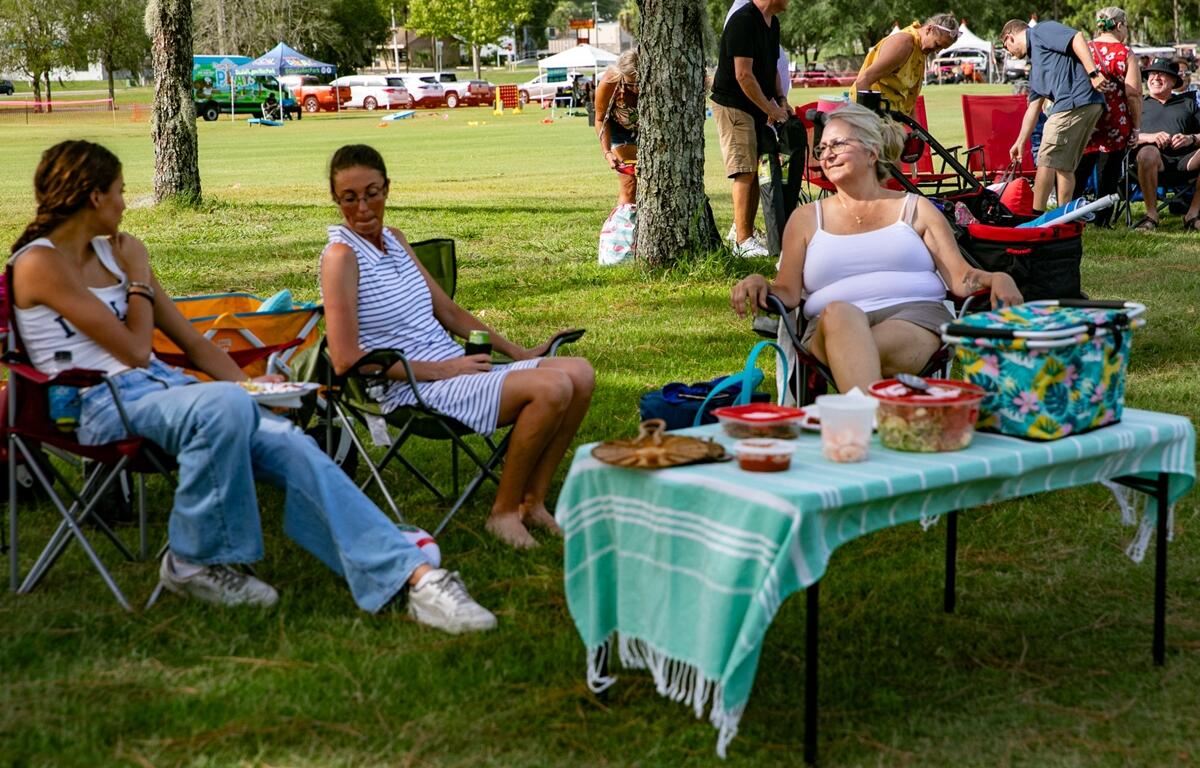 Ember Bateman, Christel Bateman, and Beth Butler sit in camp chairs around a picnic setup at Symphony Under the Stars.