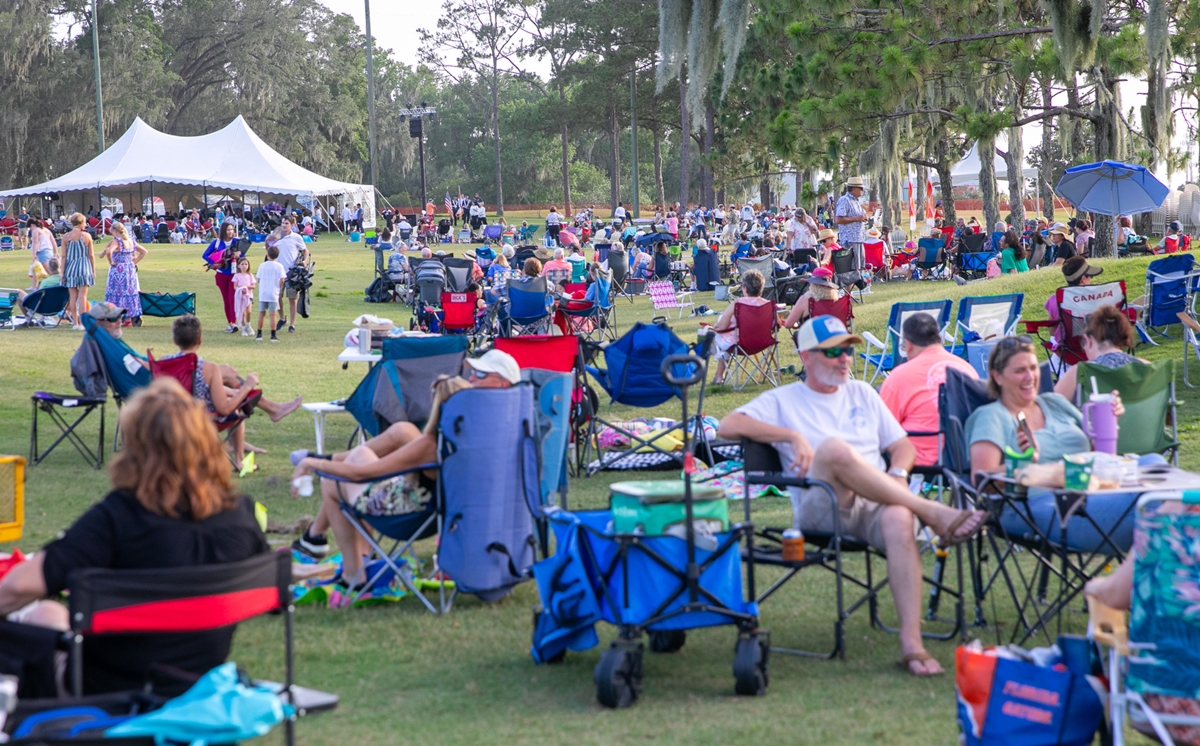 Groups of people gathered in chairs and standing on the lawn before the concert begins.