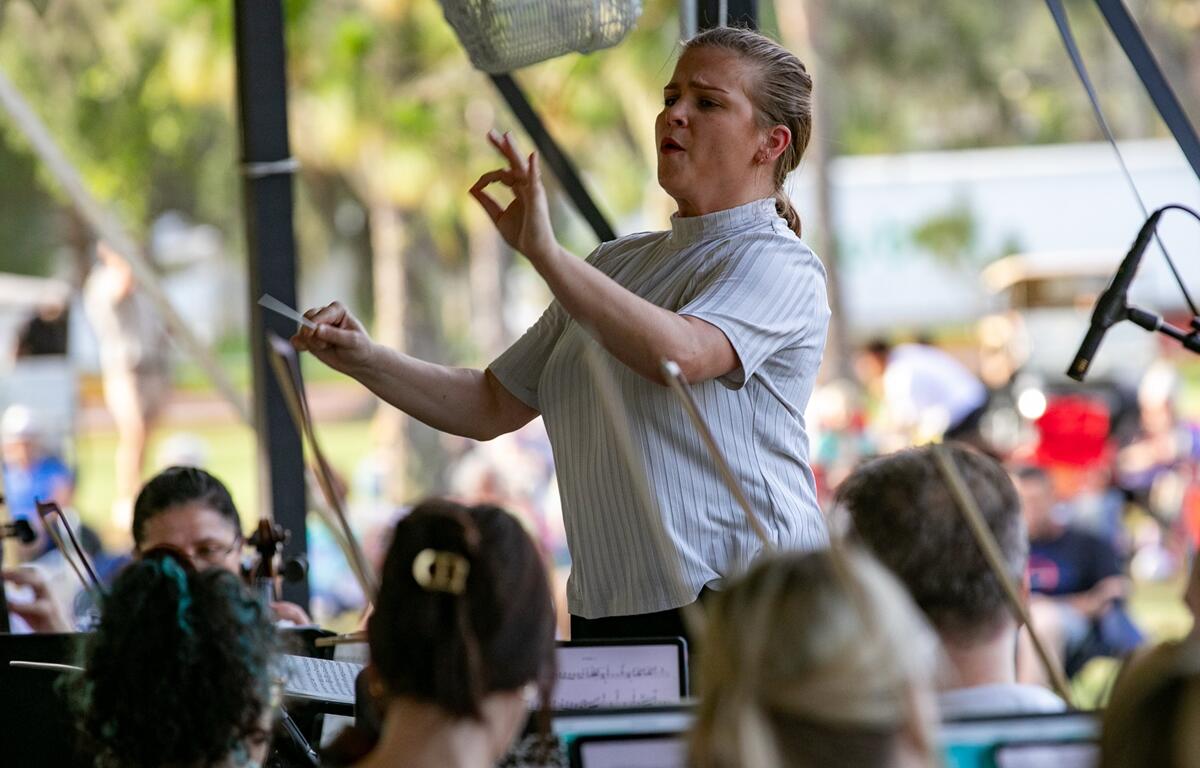 Abigail Mistretta gestures expressively while conducting the orchestra under the event tent.