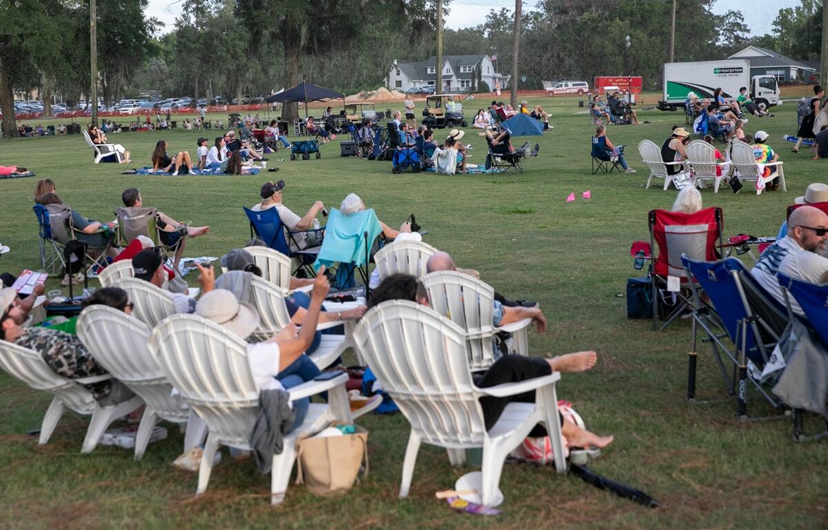 Groups of people gathered in chairs and standing on the lawn before the concert begins.