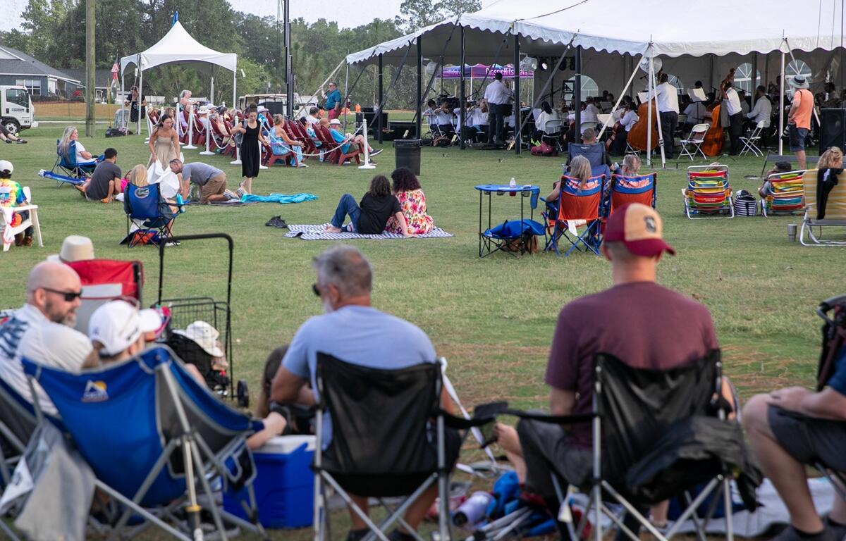 Groups of people gathered in chairs and standing on the lawn before the concert begins.