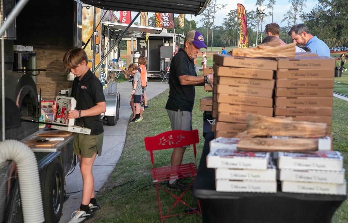 Vendors stack pizza boxes while guests wait for food during the outdoor music fundraiser.
