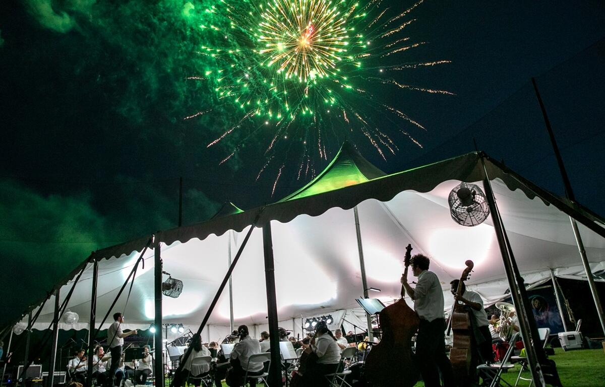 Green and gold fireworks shine above the white concert tent as the orchestra performs underneath.