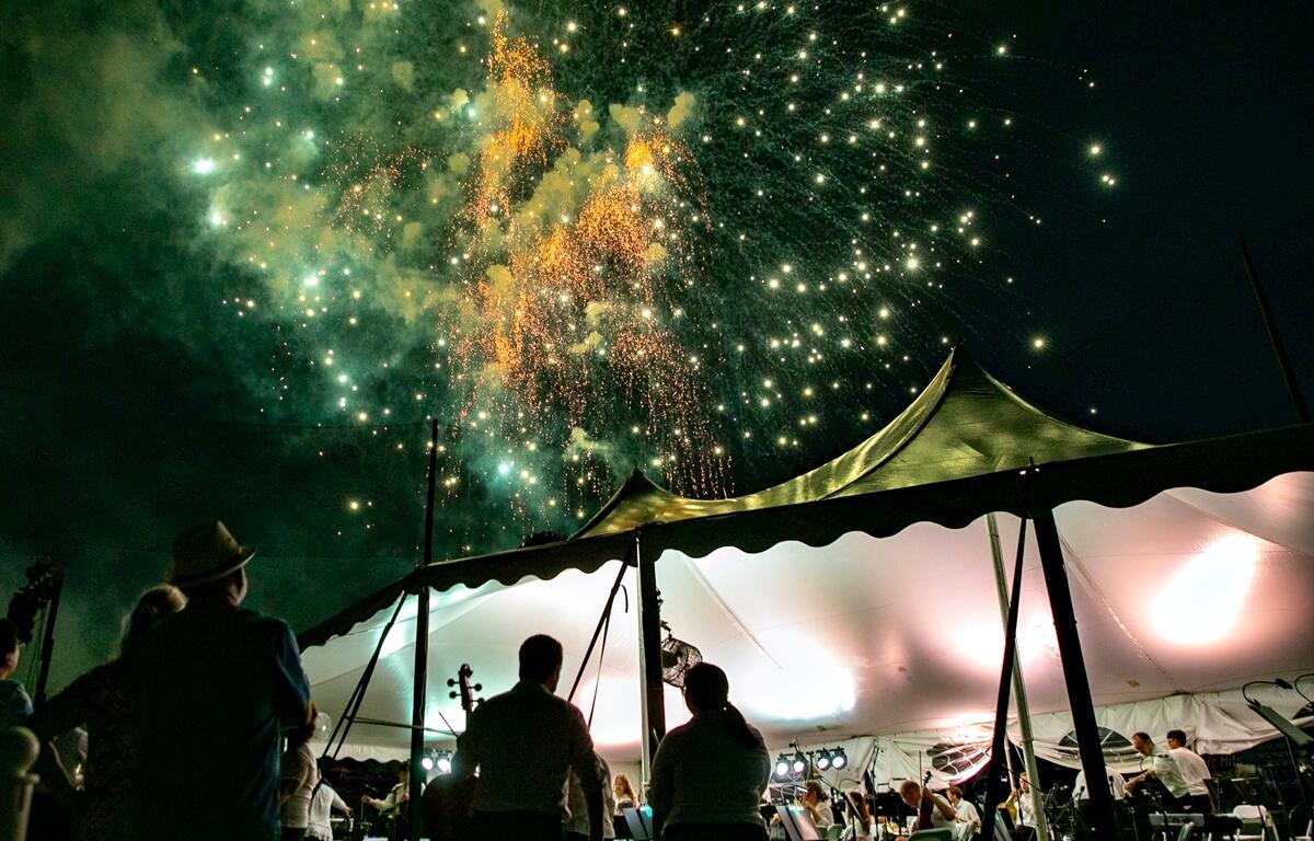 Colorful fireworks light up the sky above a large white performance tent during the Symphony Under The Stars event in Ocala.