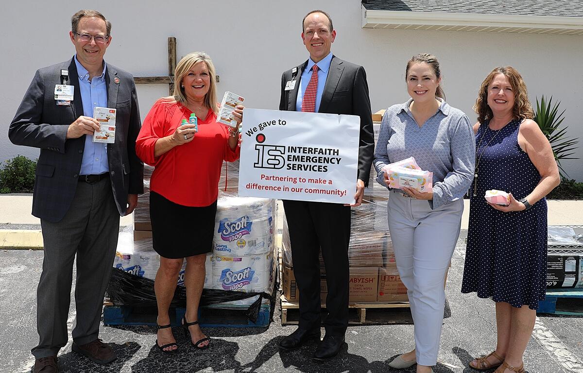 Five representatives from HCA Florida Healthcare and Interfaith Emergency Services pose with donated hygiene items outside Interfaith’s Ocala building.