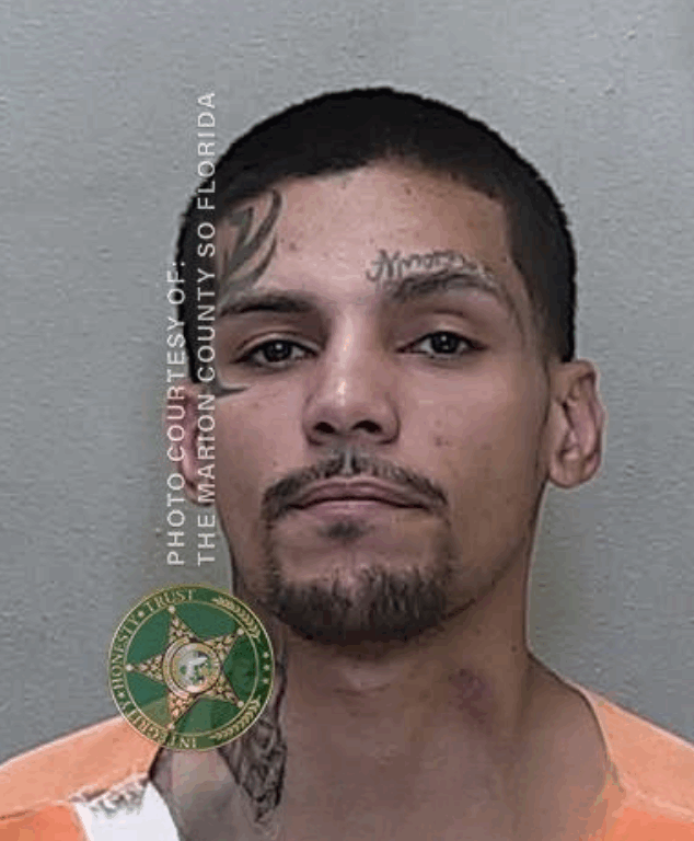 Mugshot of a younger man with short black hair, a goatee, and visible tattoos on his forehead and neck. He is wearing an orange and white jail uniform. The image includes the watermark “Photo Courtesy of: The Marion County SO Florida” and the sheriff’s office badge.