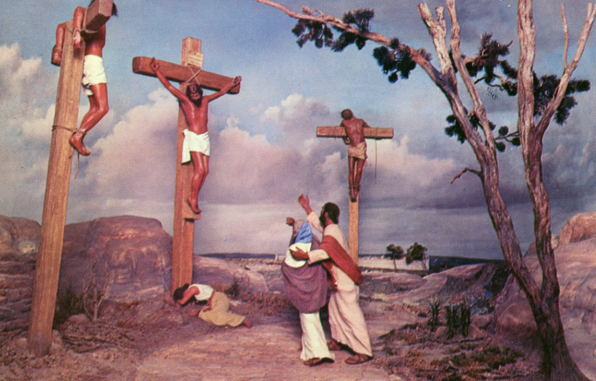 Color diorama showing Jesus on the cross with two others, set against a painted sky backdrop, part of the Prince of Peace Memorial collection.