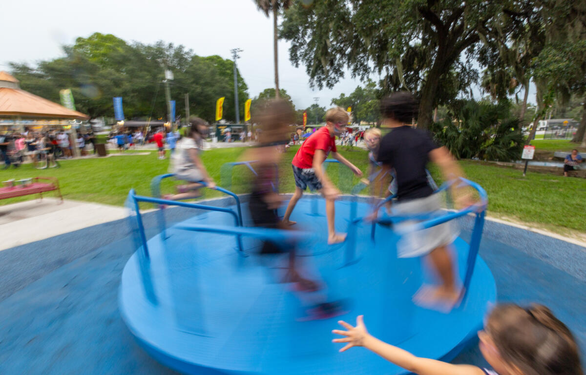 Kids in motion spin on a blue merry-go-round at a park during a Fourth of July celebration.