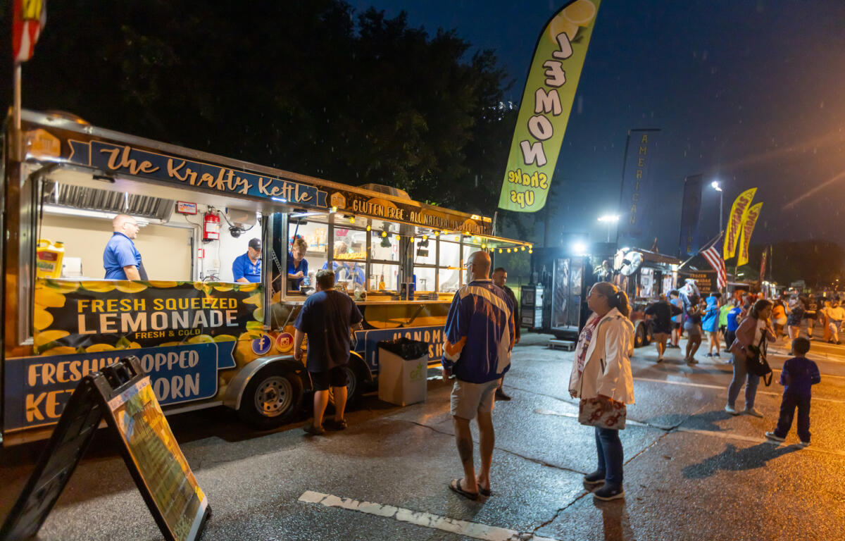 People stand in front of a lemonade and kettle corn food truck during a nighttime Fourth of July event in Ocala.