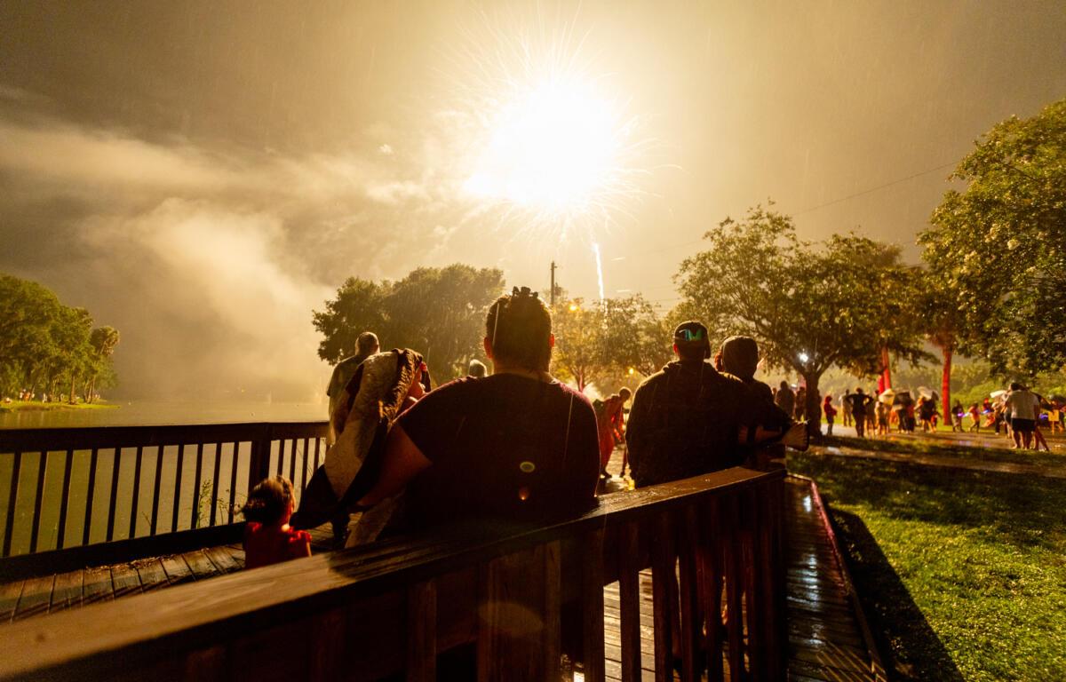 People watch a large firework burst in the rain near a lake at night during Ocala’s Fourth of July event.