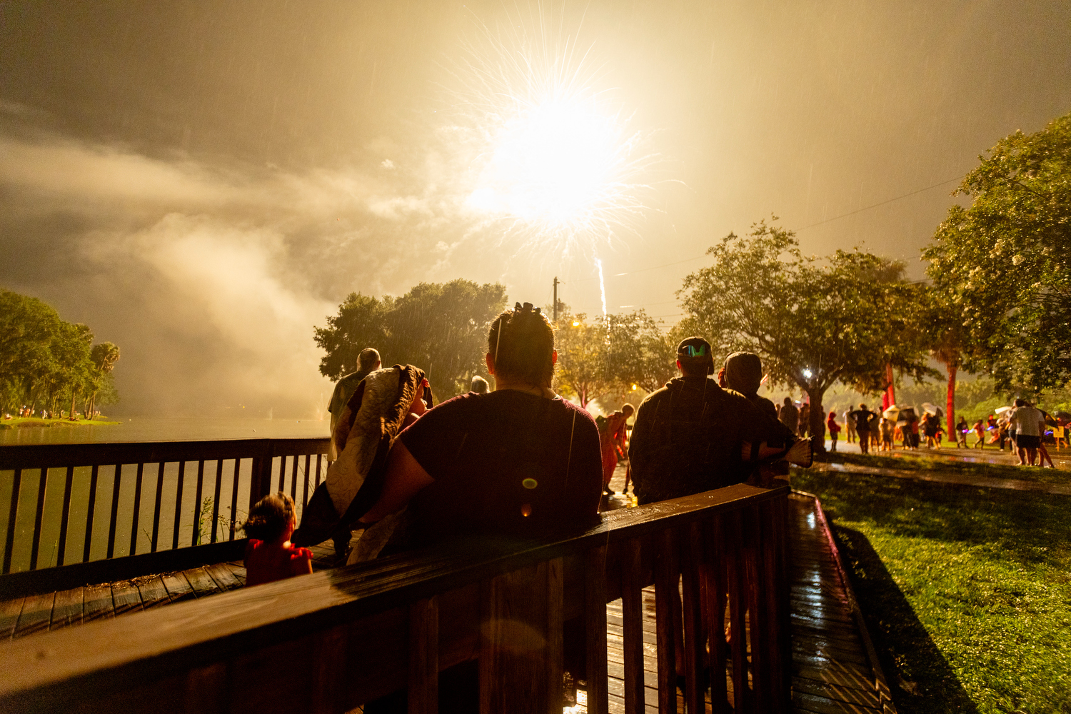 People watch a large firework burst in the rain near a lake at night during Ocala’s Fourth of July event.