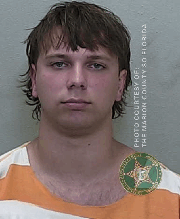 Mugshot of a younger man with shorter brown hair. He is wearing an orange and white jail uniform. The image includes the watermark “Photo Courtesy of: The Marion County SO Florida” and the sheriff’s office badge.