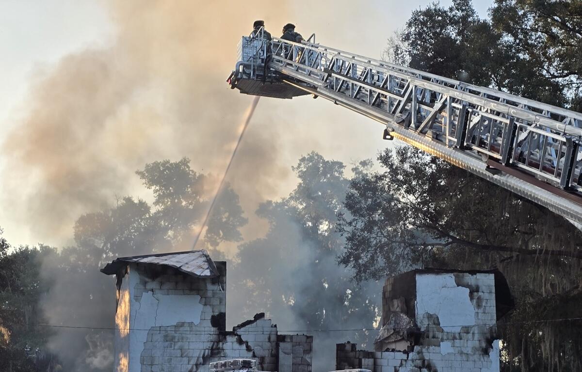 Firefighters spray water from an aerial ladder onto the charred remains of a burned church surrounded by smoke.