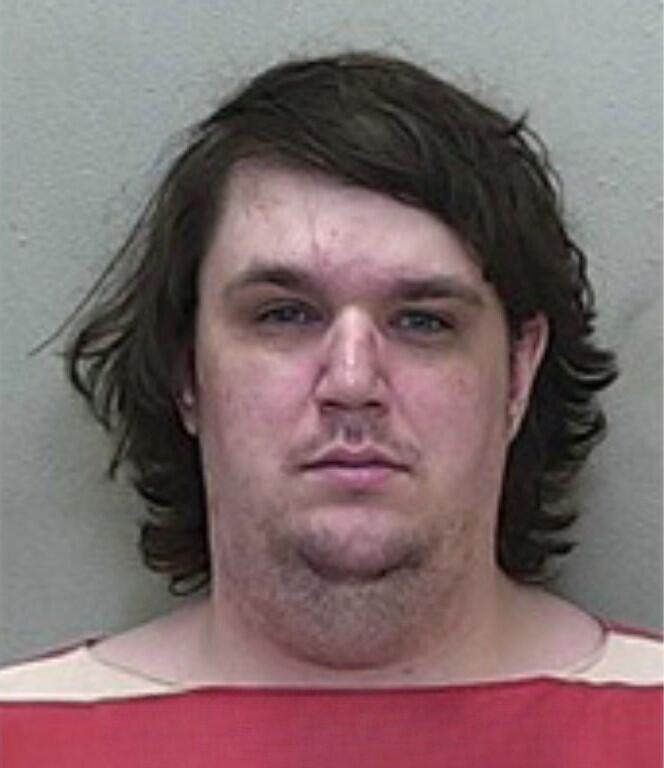Mugshot of a man with medium-length dark hair and no visible facial hair, wearing a red-and-white striped jail uniform.