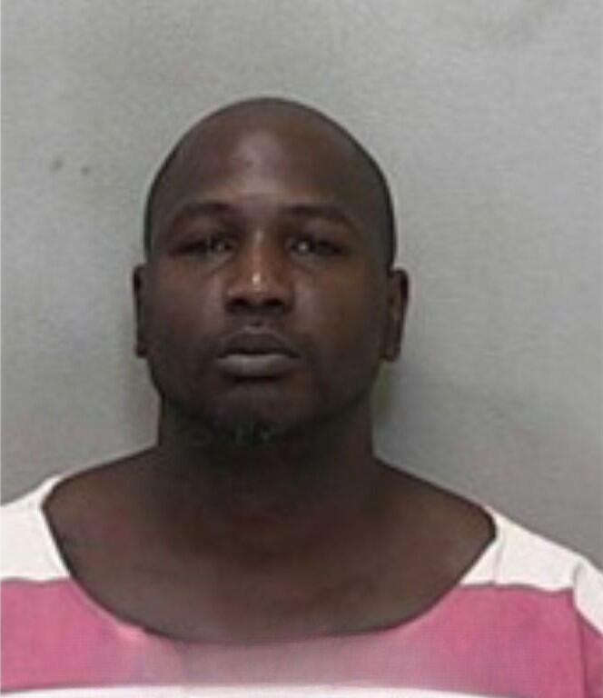 Mugshot of a bald man with a trimmed beard, wearing a red-and-white striped jail uniform.