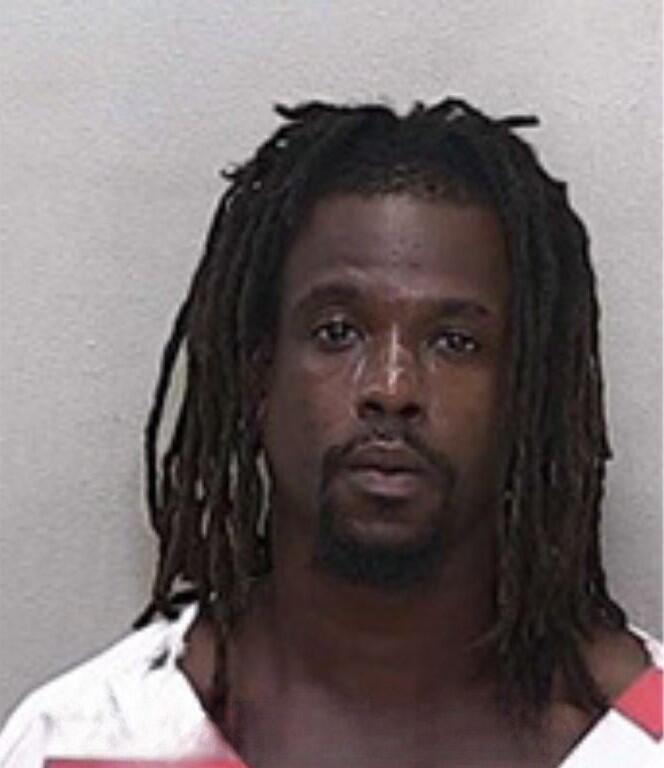 Mugshot of a man with long dreadlocks, wearing a red-and-white striped jail uniform.