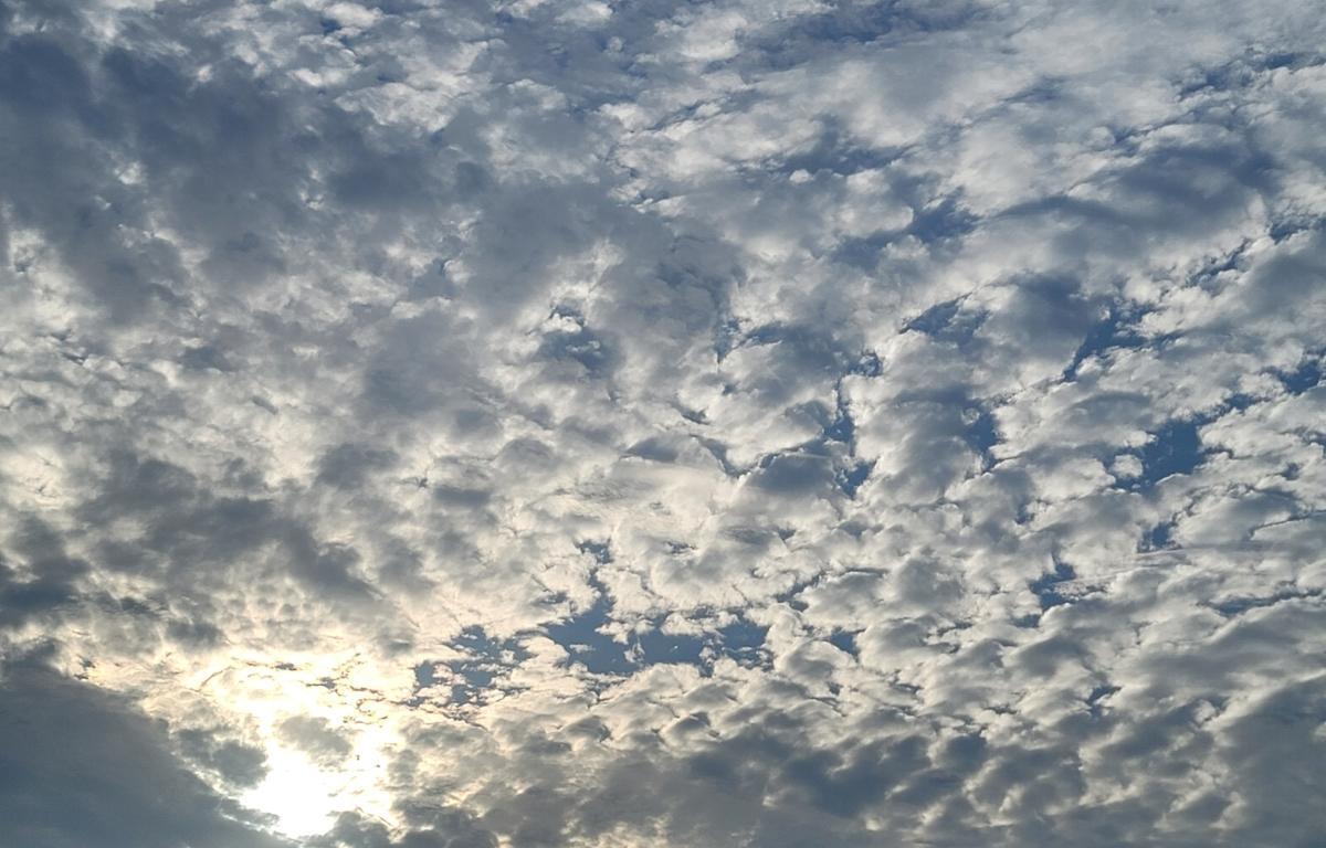 A bright blue sky covered in scattered clouds with sunlight shining faintly through them.