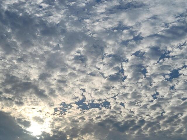 A bright blue sky covered in scattered clouds with sunlight shining faintly through them.