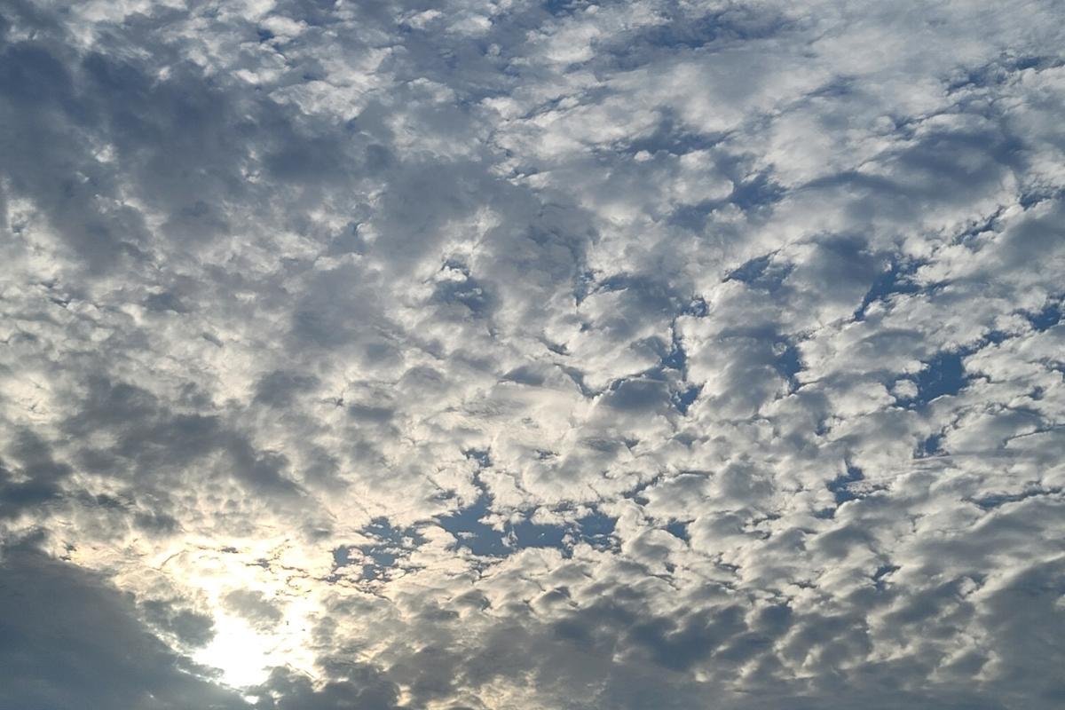 A bright blue sky covered in scattered clouds with sunlight shining faintly through them.