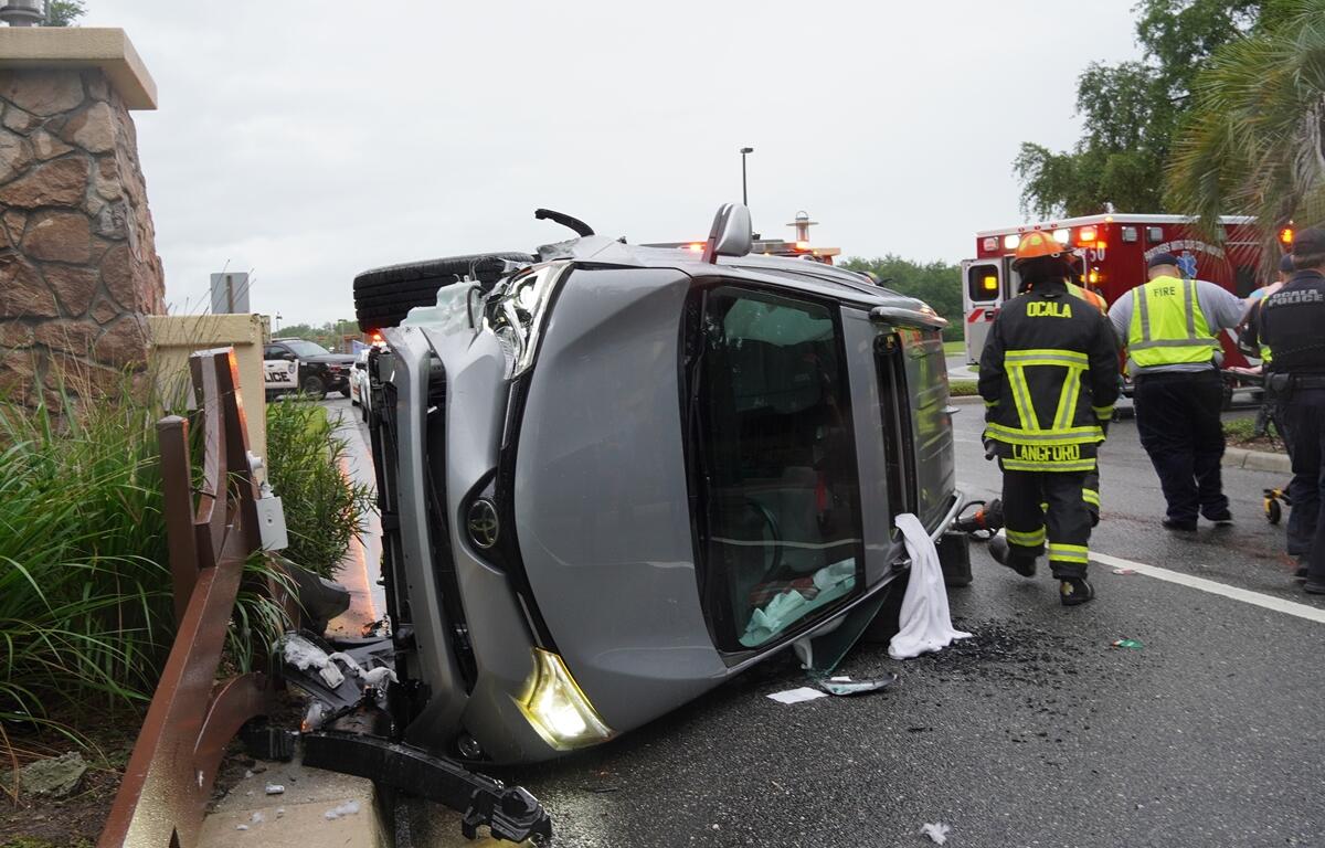 Emergency crews near a rolled-over SUV with front-end damage beside a fence.