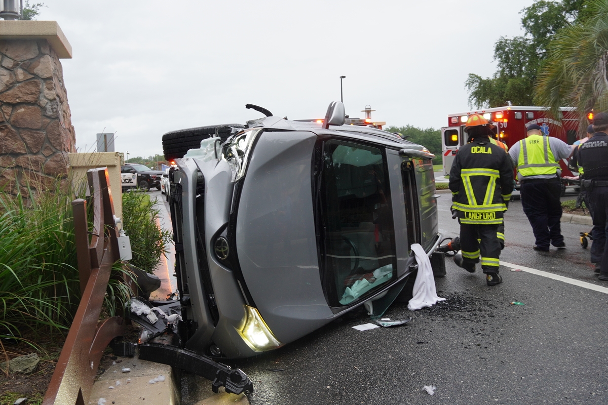 Emergency crews near a rolled-over SUV with front-end damage beside a fence.