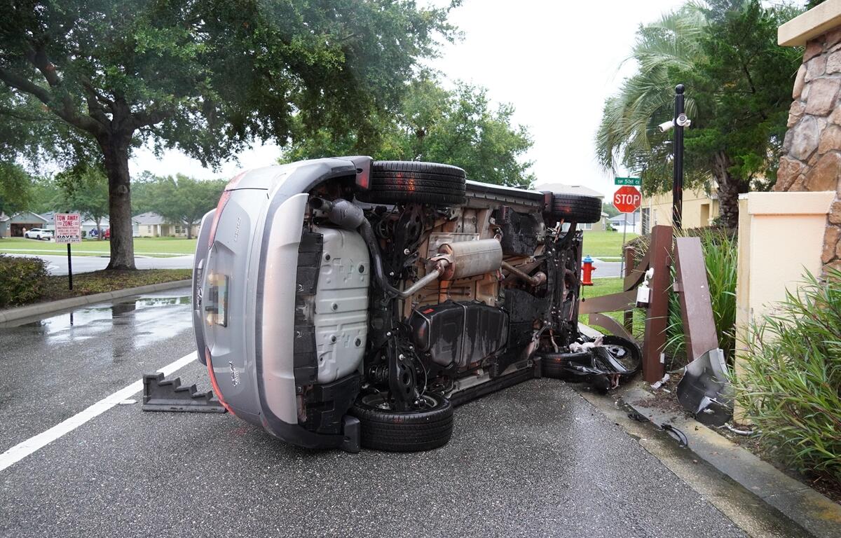 Overturned silver SUV with visible undercarriage after hitting a fence.