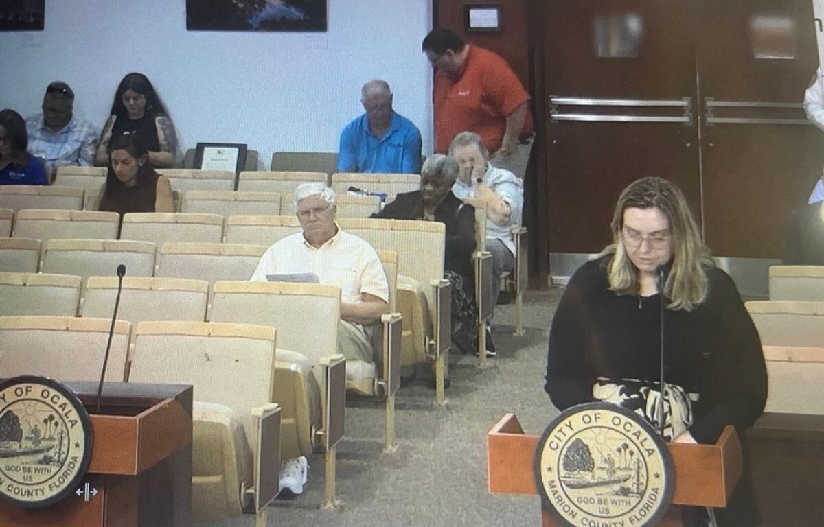 Emily Johnson speaks at a podium during an Ocala City Council meeting as attendees listen from the audience.