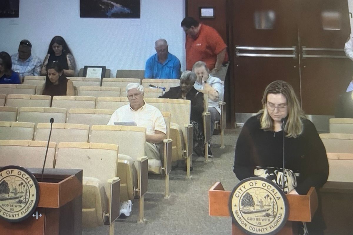 Emily Johnson speaks at a podium during an Ocala City Council meeting as attendees listen from the audience.