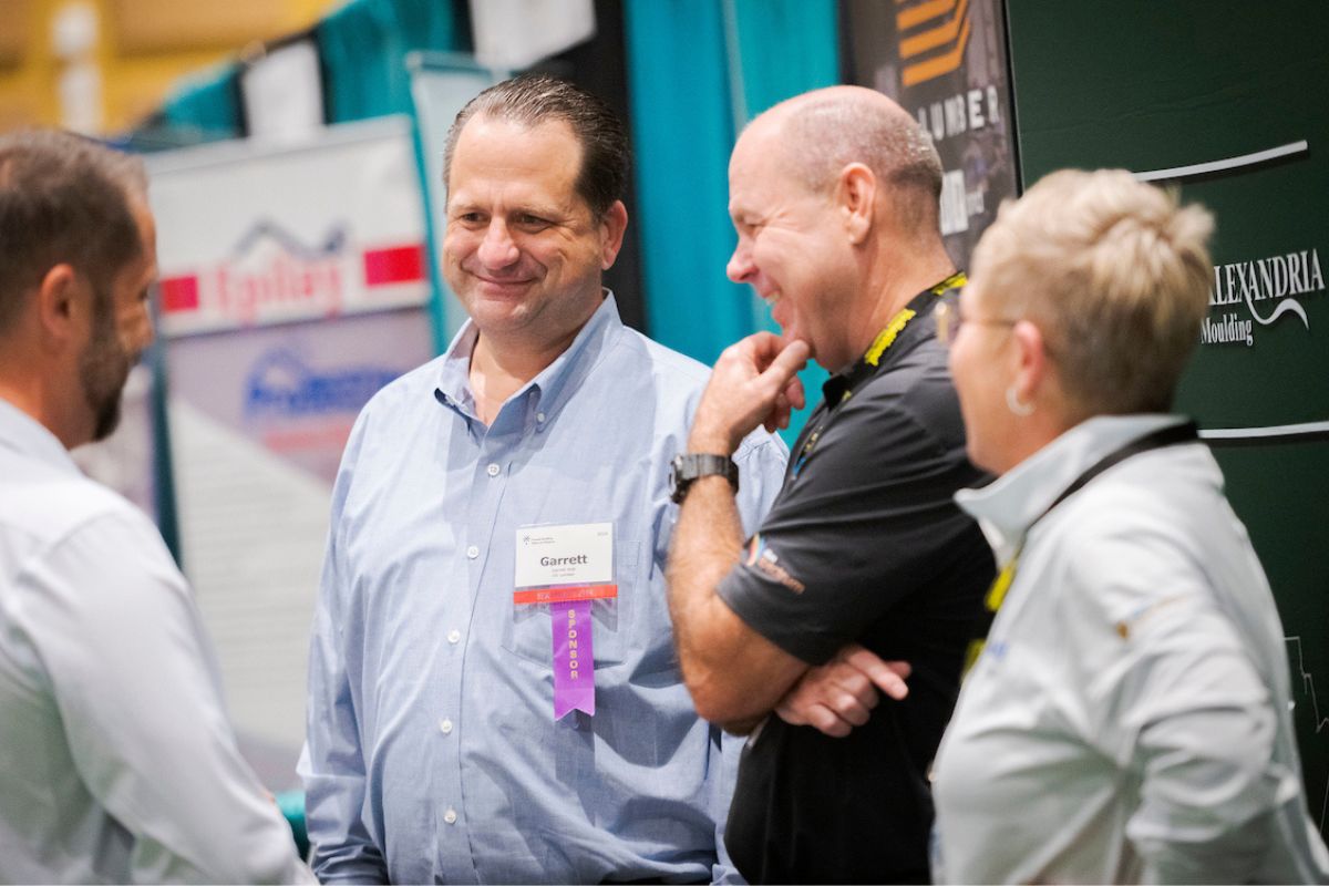 Four men talking with a trade show display in the background.