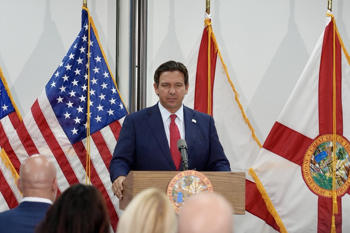 Florida Gov. Ron DeSantis speaks at a podium flanked by American and Florida state flags during a press conference.