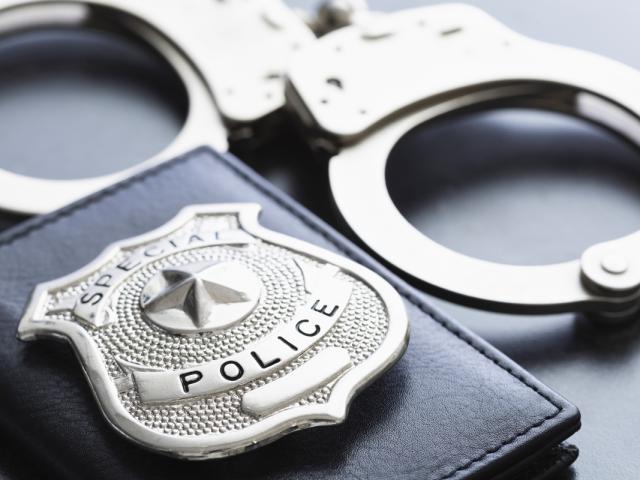 Close-up of a police badge and metal handcuffs on a dark surface.