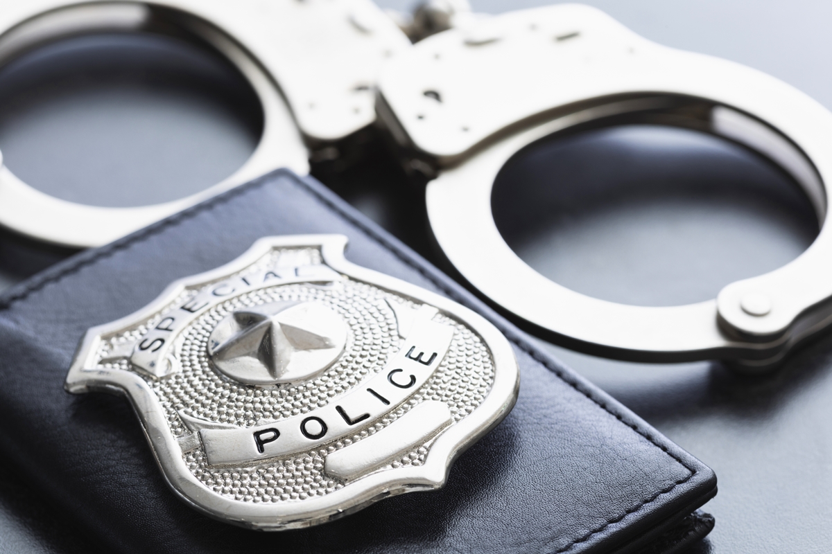 Close-up of a police badge and metal handcuffs on a dark surface.