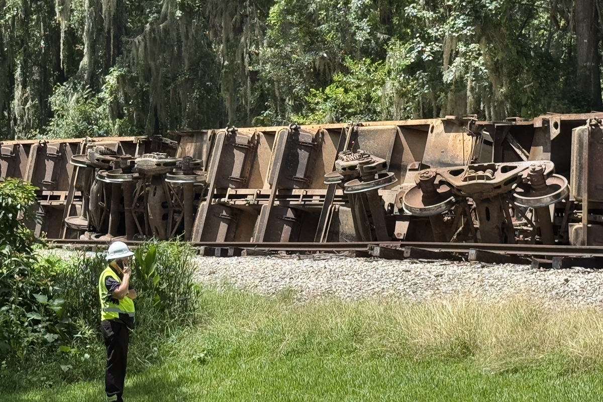 Overturned freight train cars on tracks in wooded area after Ocala derailment.