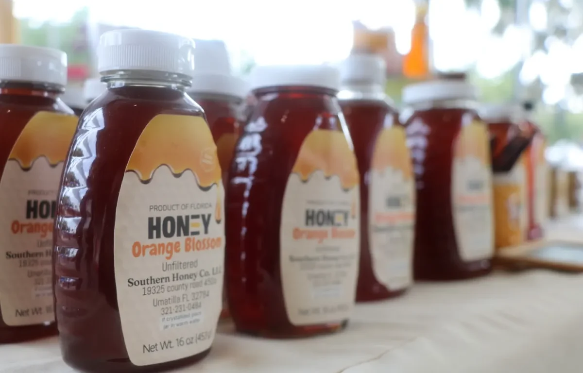 A close-up of bottles of packaged honey sit on a table with a white tablecloth.