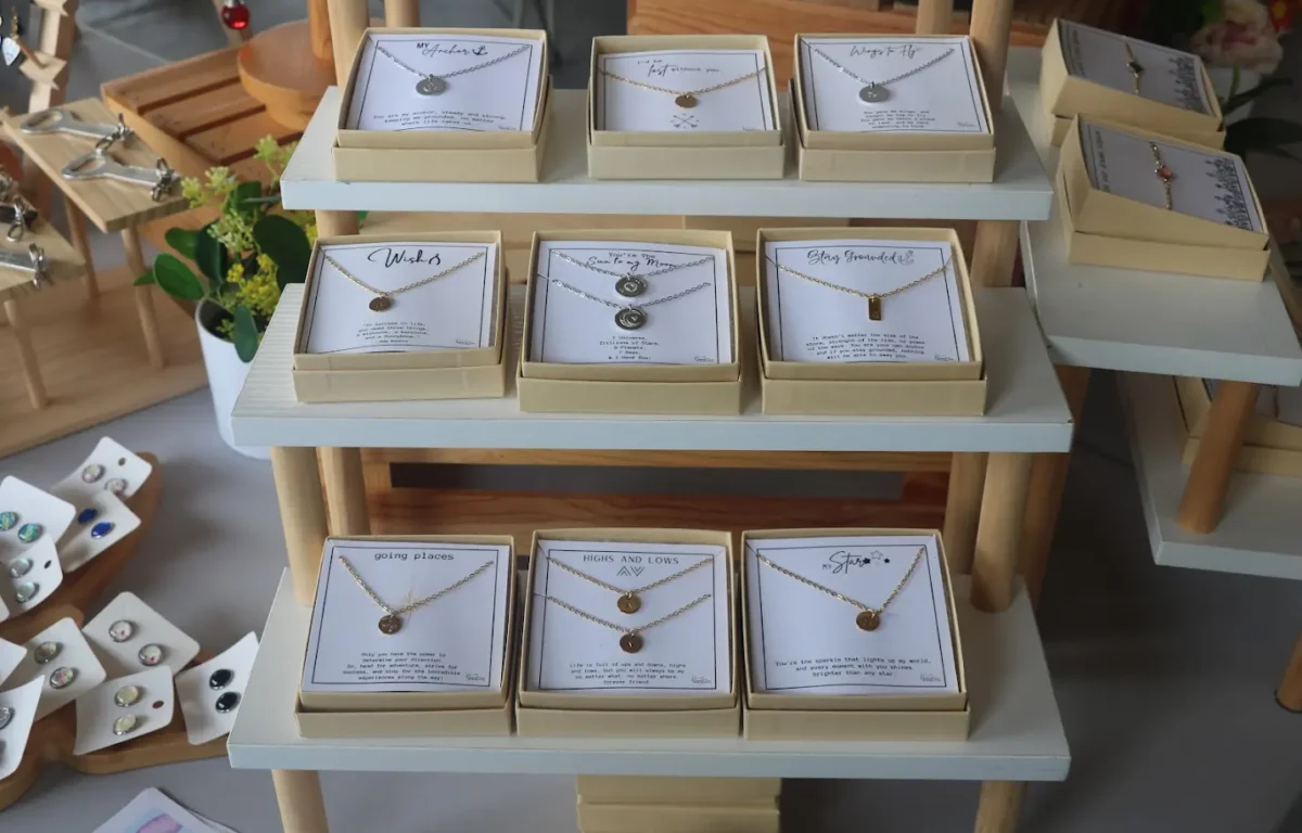 Homemade jewelry such as necklaces and earrings sit on tiered shelves and tables with decorative plants.