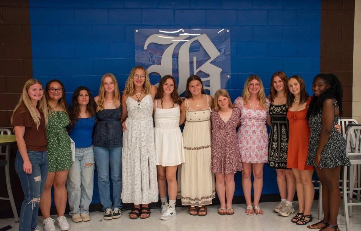 Members of the Belleview 19u Dixie Debs softball team pose in dresses for a group photo at a celebration event.